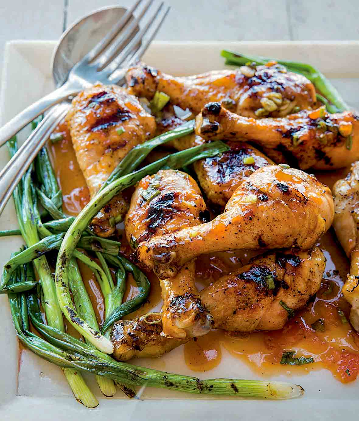 Square plate of a pile of grilled sweet and sticky sriracha drumsticks and grilled scallions