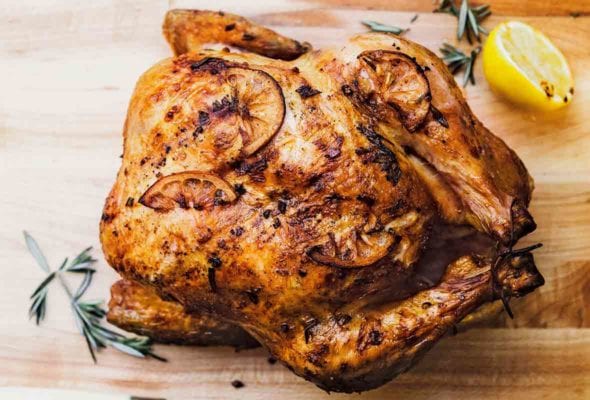 Whole roast chicken with browned lemon slices on the skin all on a cutting board