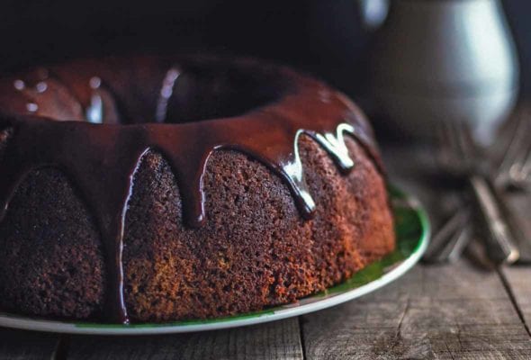A chocolate zucchini cake glazed with chocolate icing on a green plate on a wooden table