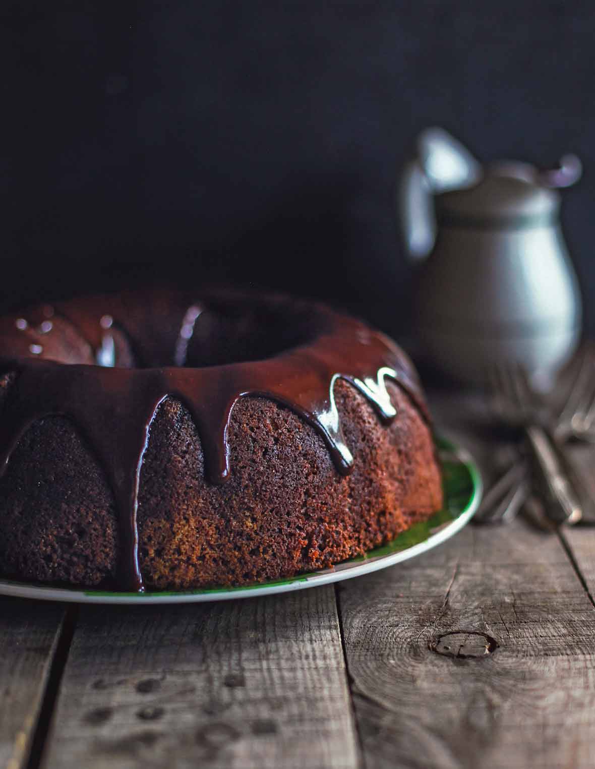 A chocolate zucchini cake glazed with chocolate icing on a green plate on a wooden table