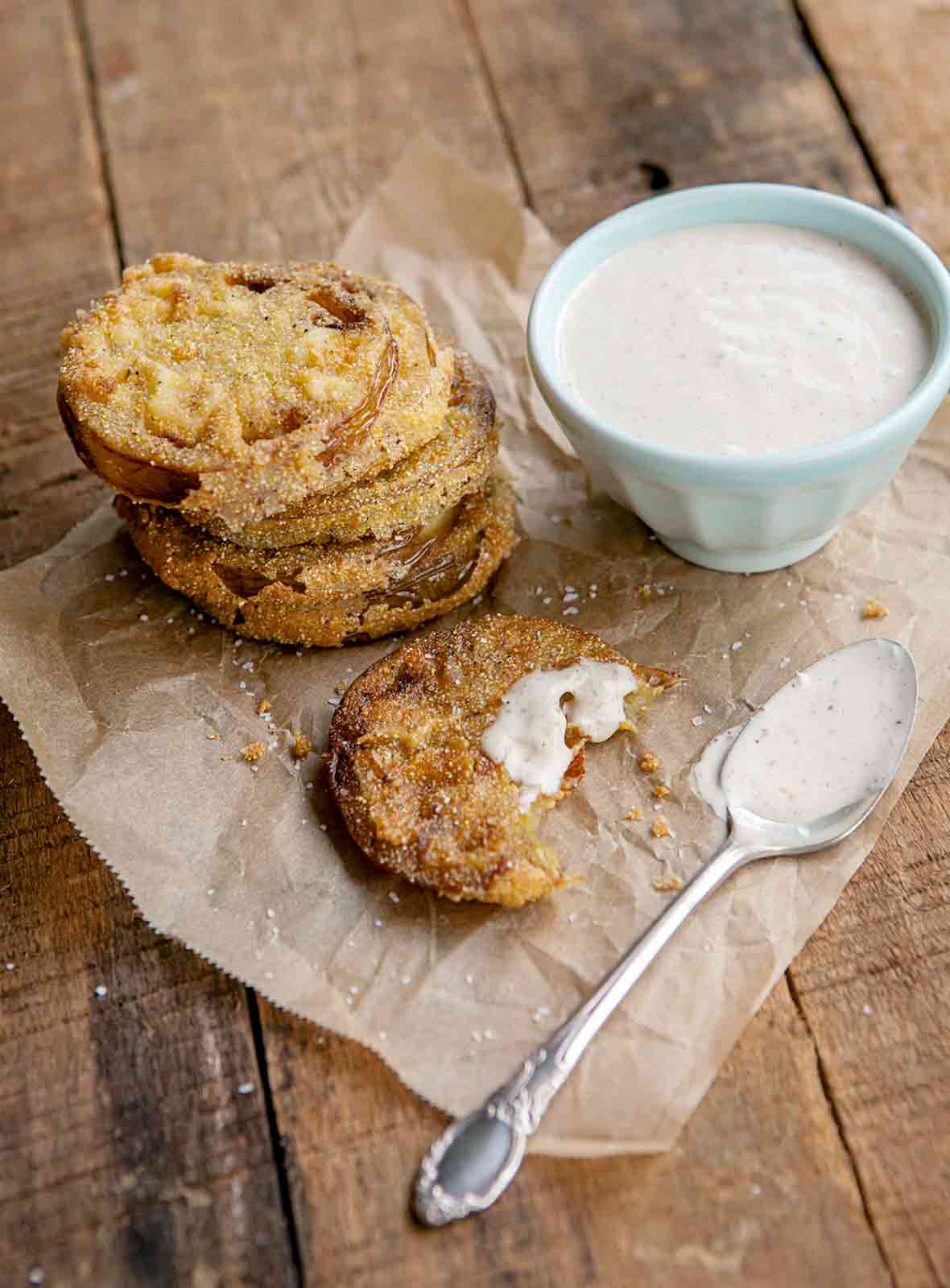 Slices of fried green tomatoes on a sheet of brown paper, on the side is a creole remoulade