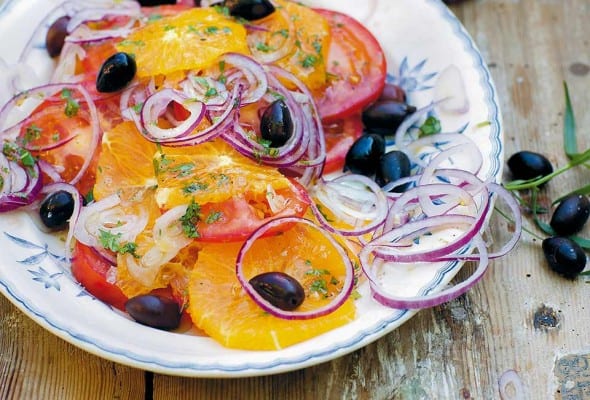 A patterned plate topped with a Moroccan salad made with sliced oranges and tomatoes, black olives, and sliced red onion.