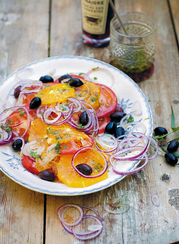 A patterned plate topped with a Moroccan salad made with sliced oranges and tomatoes, black olives, and sliced red onion.
