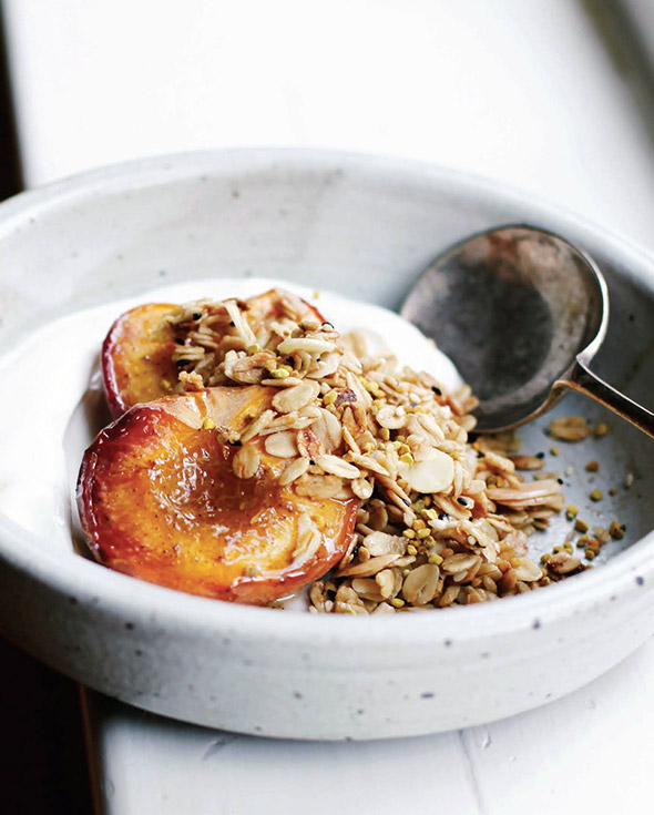 A white bowl of roast peaches topped with an easy granola of oats and almonds, Greek yogurt underneath