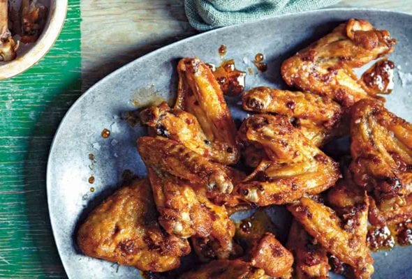 A platter of Spanish-style deep-fried chicken wings on a wooden table with a bowl of wing bones on the side.