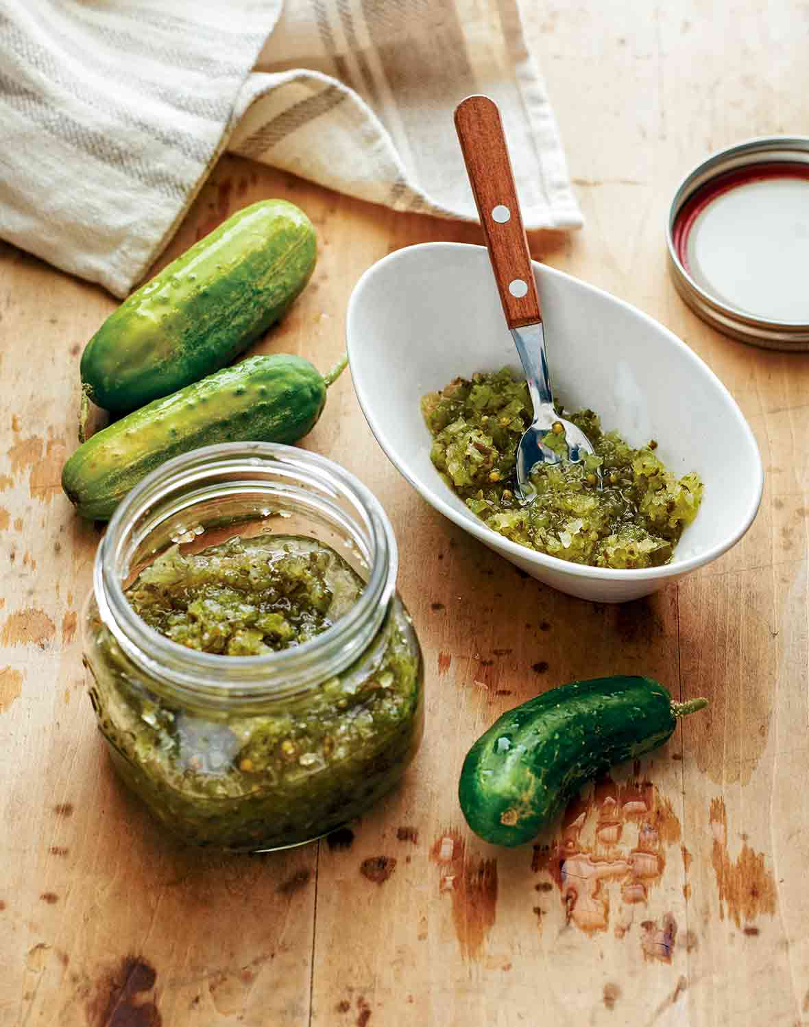 A white bowl and a mason jar of sweet pickle relish on a wooden table
