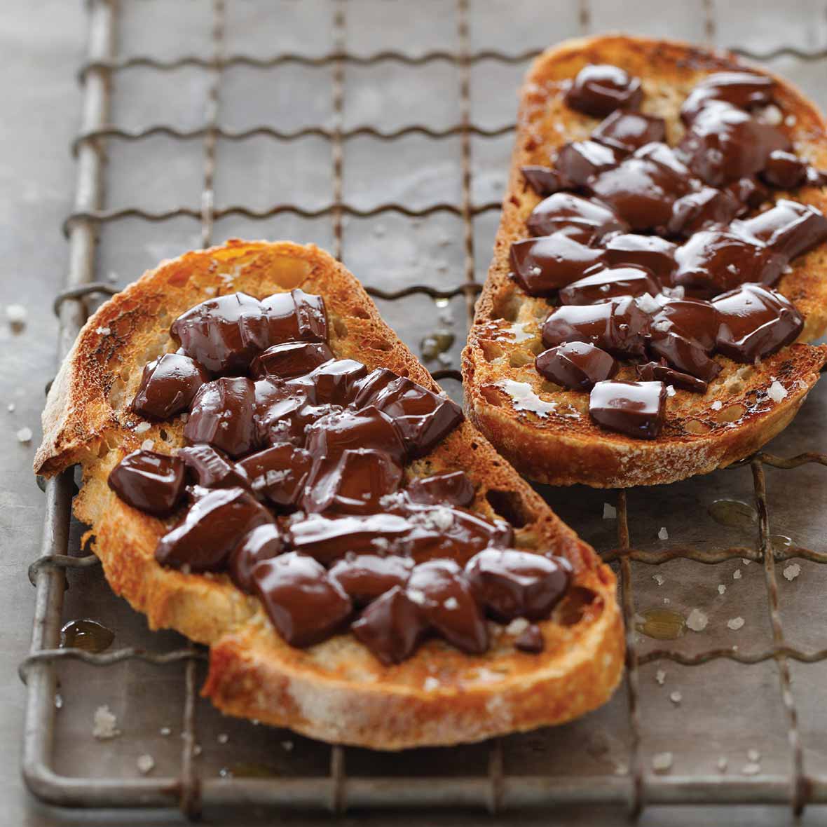 Two slices of chocolate sandwich, made with toasted French bread, chocolate, and a sprinkling of salt on a wire rack.