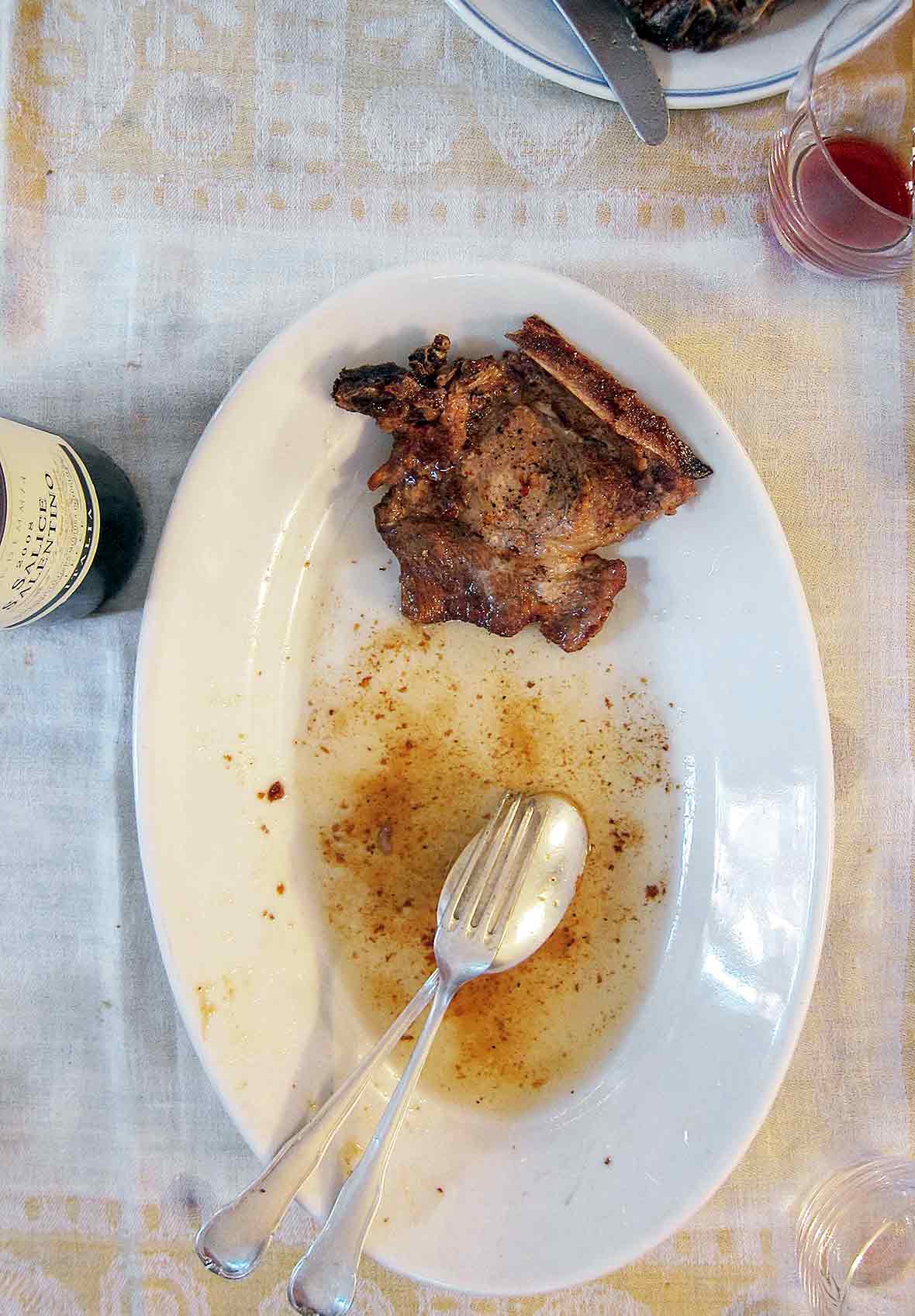 Oval plate with a salt and pepper pork chop, spoon, fork, and juice on it