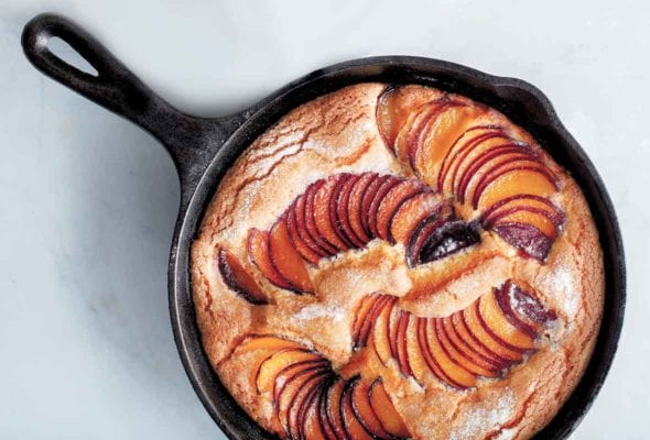 A cast-iron skillet with a golden cake with slices of fanned out plums baked in