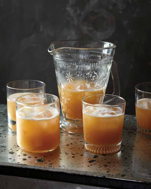 A pitcher and 4 tumblers filled with amber colored whiskey sour