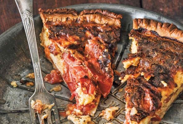A metal pie plate with two cut slices of roasted tomato quiche and a fork resting beside them.