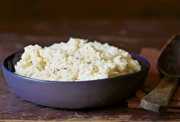 A blue bowl of cauliflower purée on a wooden table