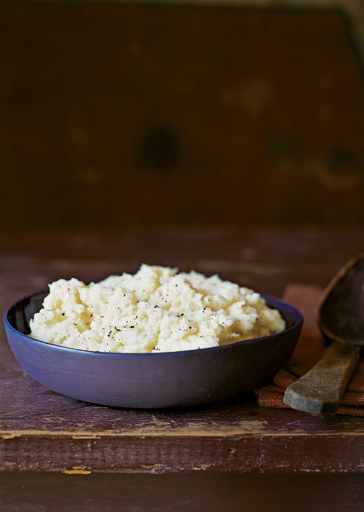A blue bowl of cauliflower purée on a wooden table