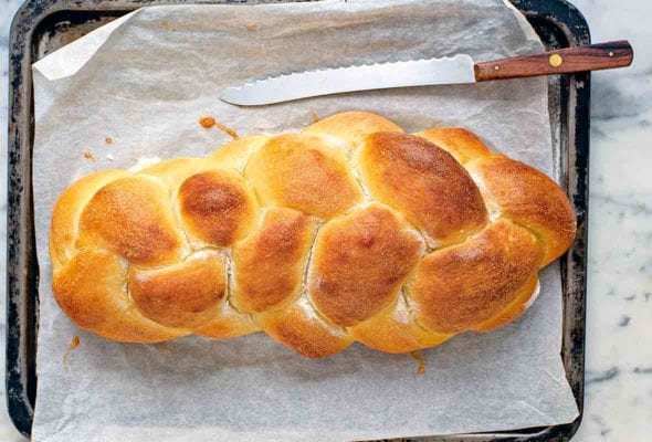 A loaf of braided challah bread on a baking sheet with a serrated knife