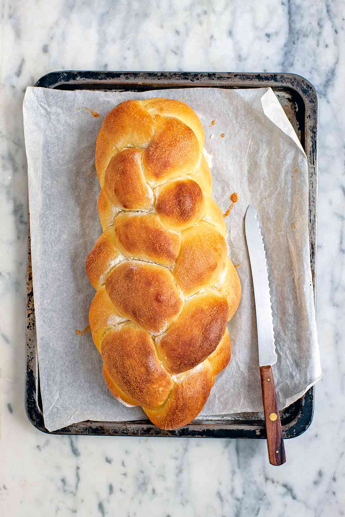 A loaf of braided challah bread on a baking sheet with a serrated knife