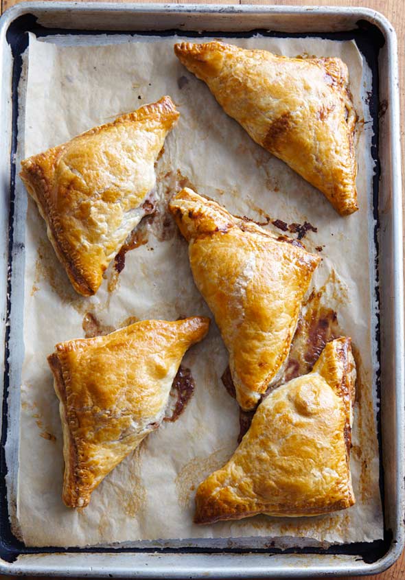 Five pear turnovers on a piece of parchment in a rimmed baking sheet.