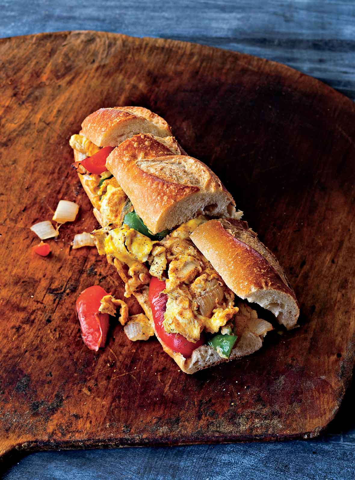 A pepper and egg sandwich on a wooden table with pieces of pepper and onion falling out.