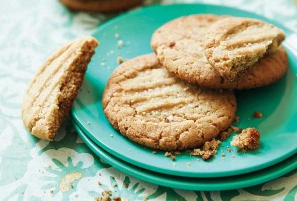 Two and a half bacon fat peanut butter cookies on two stacked green plates with a stack of cookies in the background.