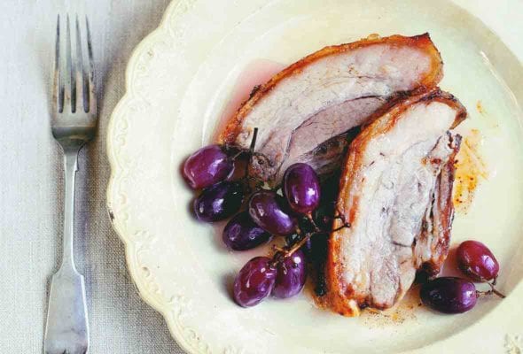 A decorative plate with two slices of roast pork and three bunches of pickled grapes.