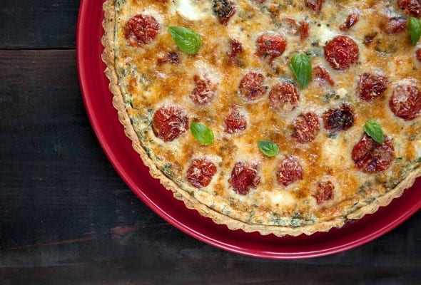 A cooked tomato cheese tart with a herbed crust on a red plate.