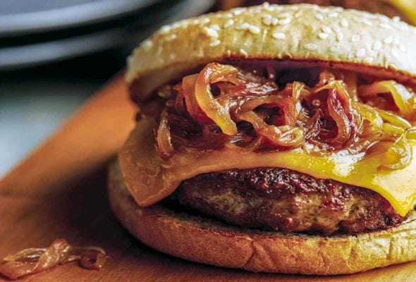 A turkey burger with maple caramelized onions and cheese on a wooden cutting board