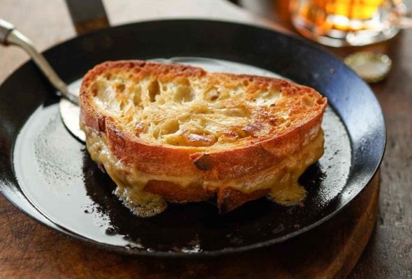 A black metal skillet with a spatula ready to flip a Welsh rarebit grilled cheese sandwich.