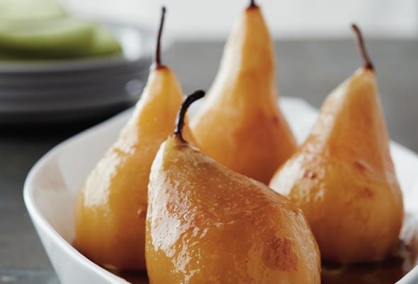 Four wine-poached pears in a white baking dish.
