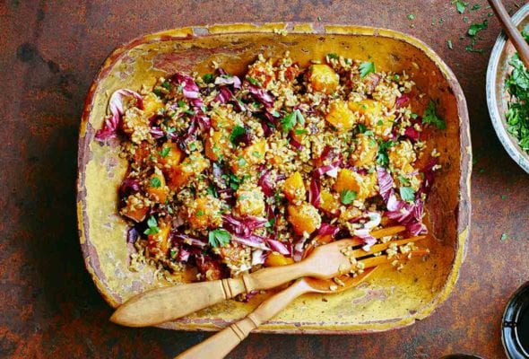 A wooden bowl with butternut squash and whole grain salad with a bowl of chopped parsley on the side and two glasses.