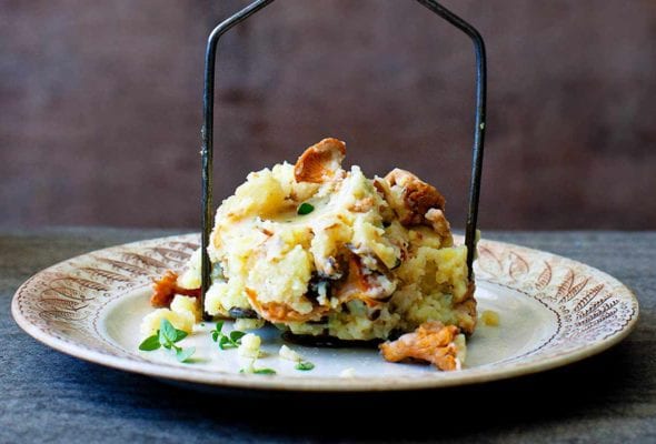 A pile of chanterelle mashed potatoes on a potato masher on a decorative plate.