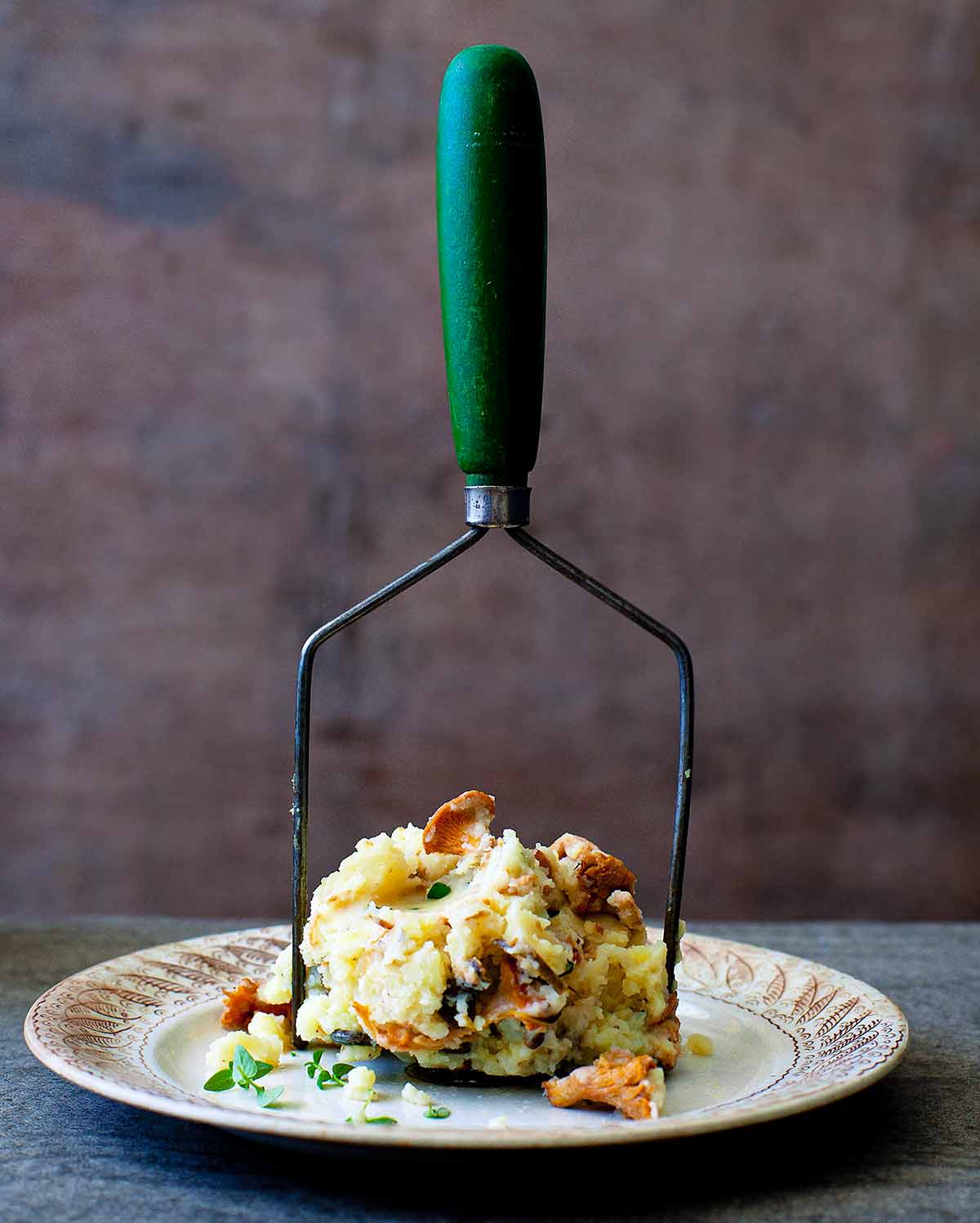 A pile of chanterelle mashed potatoes on a potato masher on a decorative plate.
