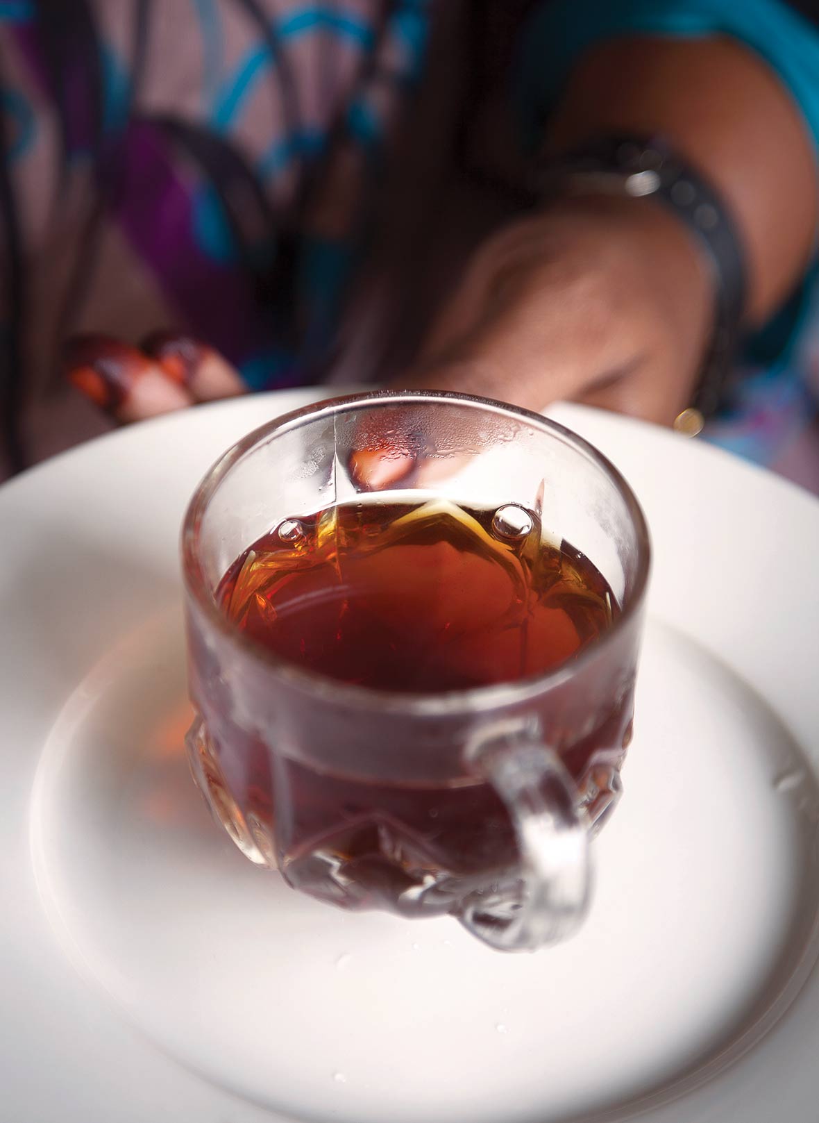 A person holding a glass mug of cinnamon tea on a white plate.