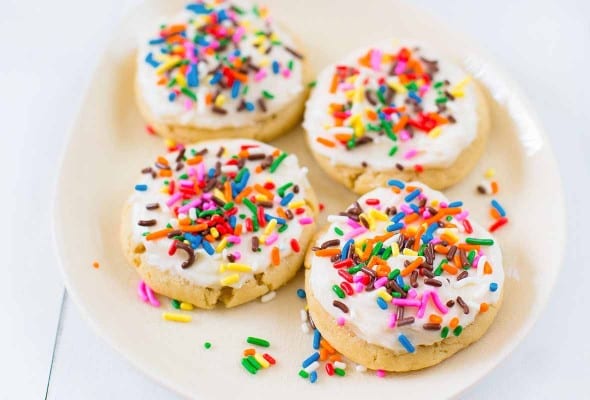Four sugar cookies topped with frosting and sprinkles on a white plate.
