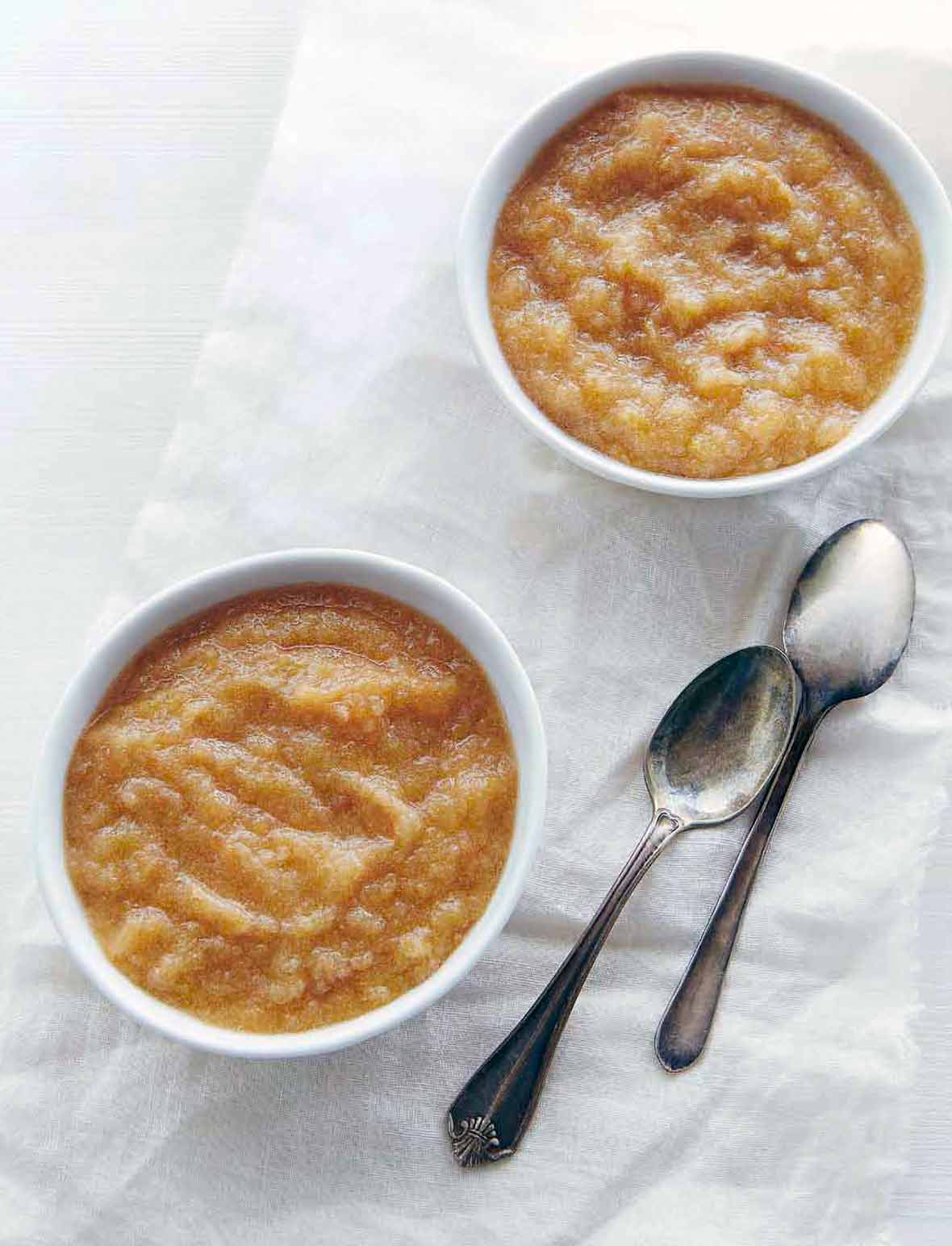 Two bowls of slow cooker applesauce with two spoons nearby