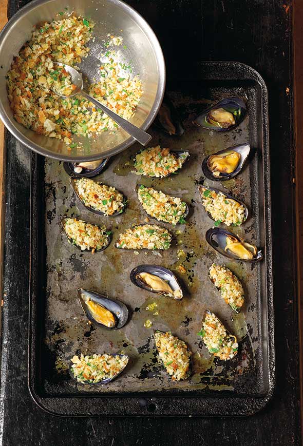A rimmed baking sheet with stuffed broiled mussels and a bowl of filling on the side