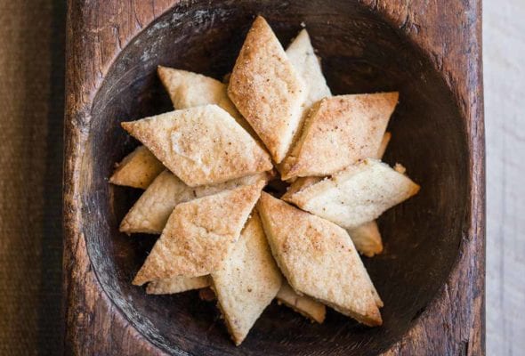 A pile of diamond-shaped biscochitos in a wooden bowl.