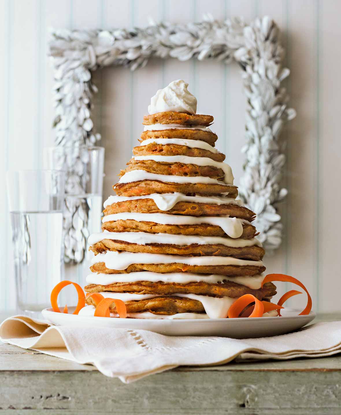 A stack of carrot cake pancakes layered with mascarpone frosting, shaped to look like a Christmas tree on a white plate.
