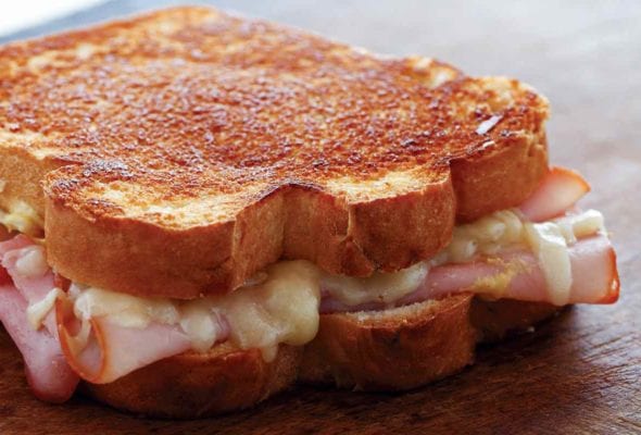 A grilled ham and cheese sandwich on a wooden cutting board.