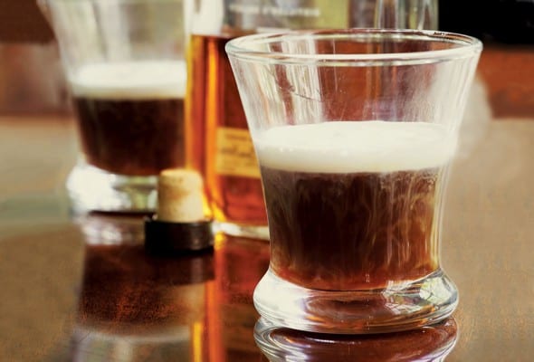 Two tumblers filled with amber liquid and a bottle of bourbon in the background