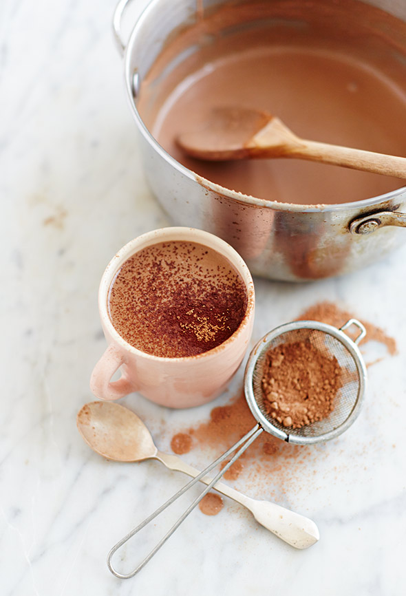 A pot and a mug filled with paleo hot cocoa and a sifter of cocoa powder on the side