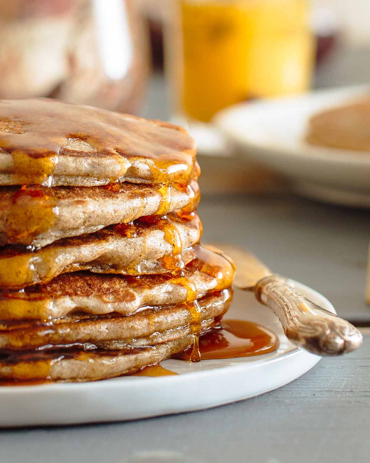 A stack of buckwheat pancakes drizzled with maple syrup on a white plate.
