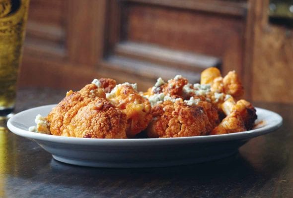 Plate of roasted cauliflower brushed with hot sauce and topped with crumbled blue cheese in front of a door