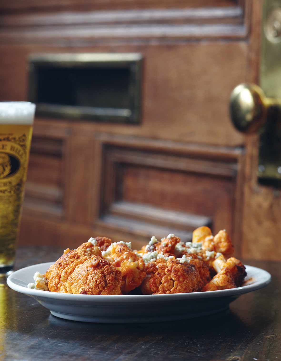 Plate of roasted cauliflower brushed with hot sauce and topped with crumbled blue cheese in front of a door