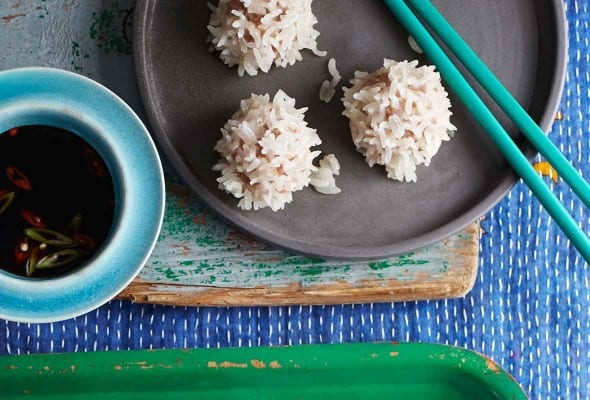 Several pork meatballs on a parchment lined green tray, and a gray plate with chopsticks on it.