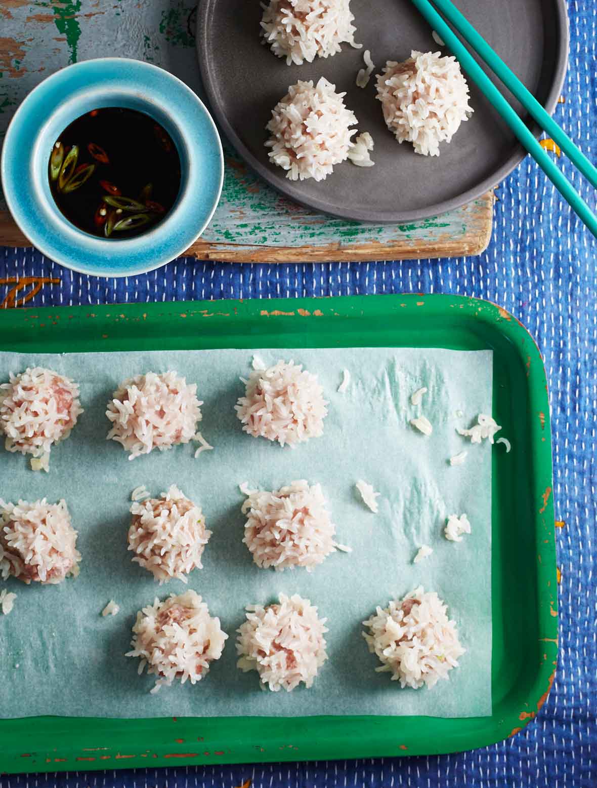Several Chinese pork meatballs on a parchment lined green tray, and a gray plate with chopsticks on it.