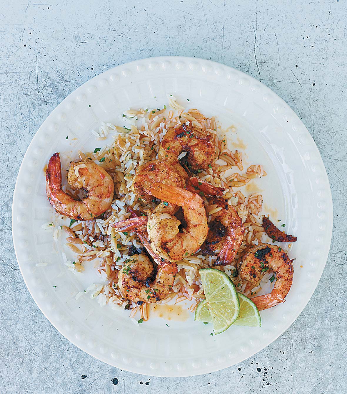A white plate topped with sauteed shrimp, rice, and lime wedges.