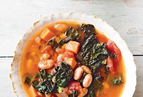 Two white bowls of Tuscan bean soup on a white surface.