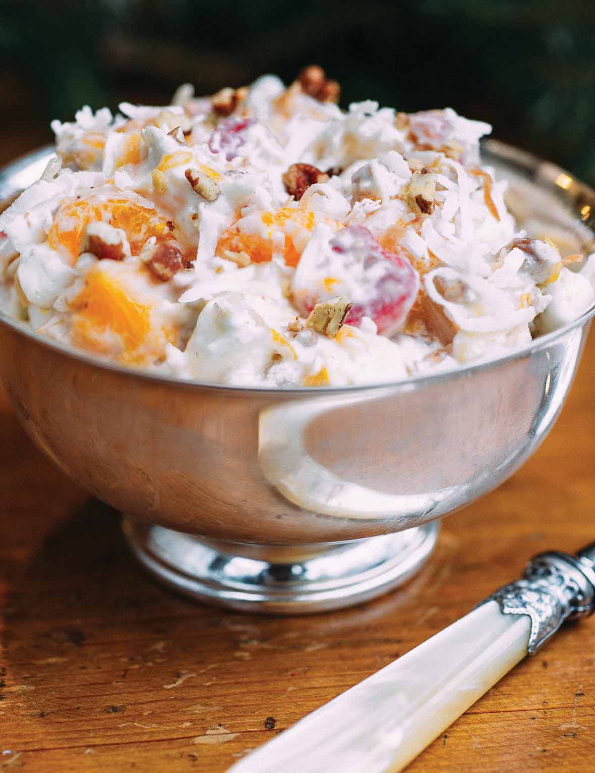 A silver bowl filled with ambrosia salad with a bone-handle knife beside the bowl.