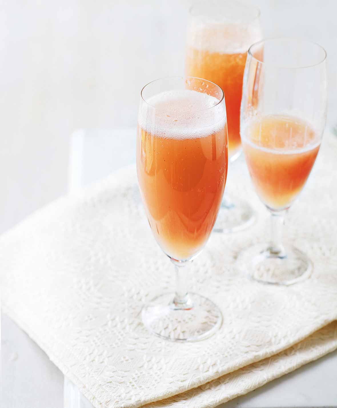 Three champagne flutes filled with classic bellini on a napkin.