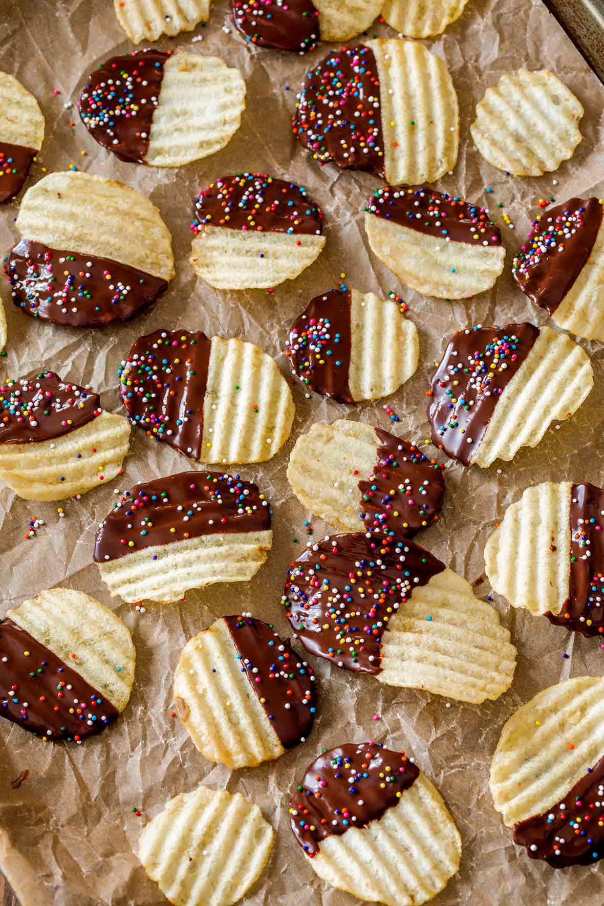 A layer of chocolate covered potato chips on a piece of parchment on a rimmed baking sheet.