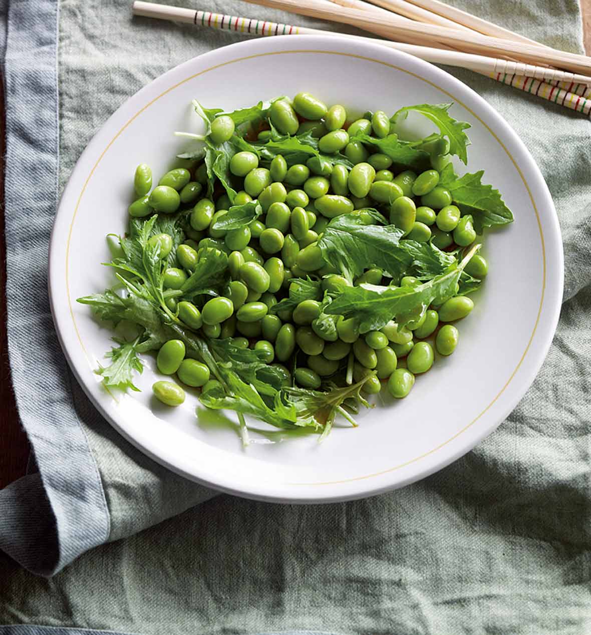 A white bowl filled with edamame salad sitting on a grey linen napkin with chopsticks on the side